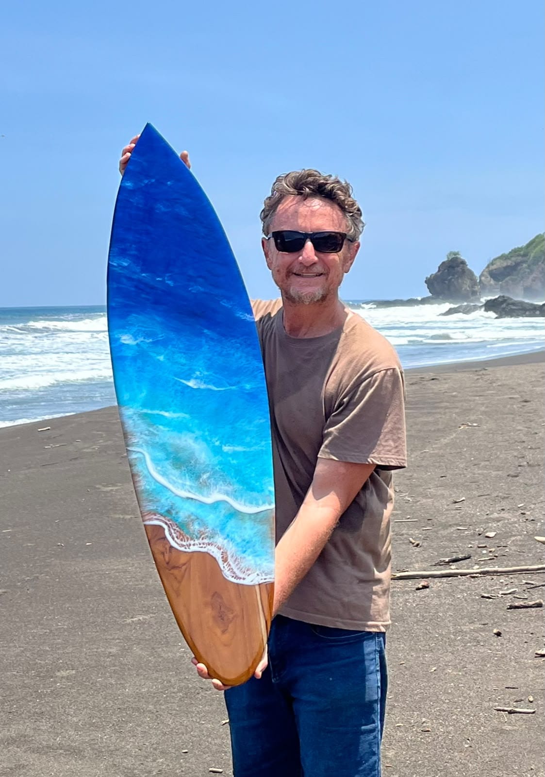 Artista sosteniendo una tabla de surf de madera y resina en la playa